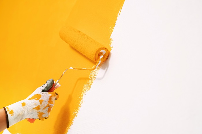 gloved-hand-using-a-roller-to-paint-a-wall-bright-yellow